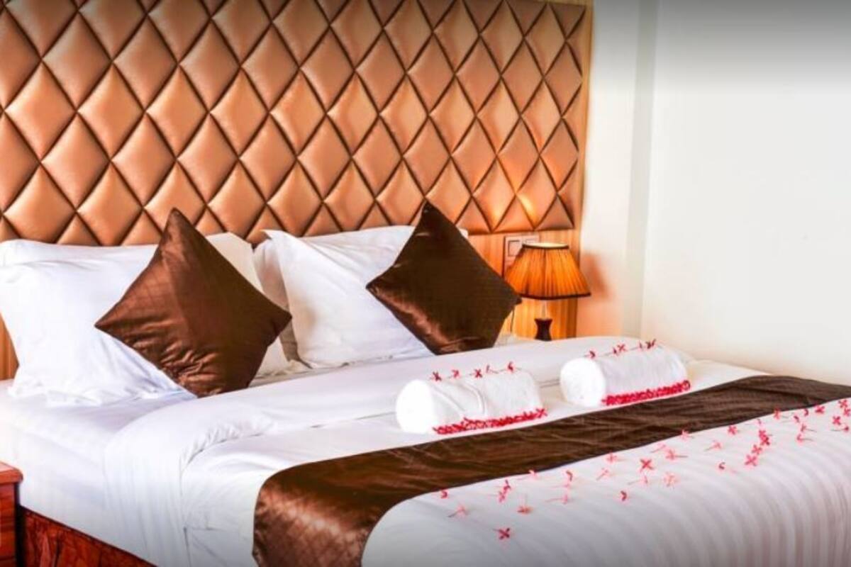 Ein Hotelzimmer mit einem gesteppten Kopfteil, weißer Bettwäsche, braunen Kissen und einer dekorativen, rot-weißen Tagesdecke.