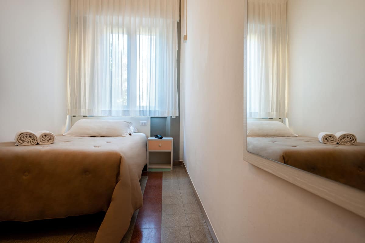 A hotel room with two beds, a nightstand, and a mirror reflecting the room.