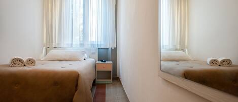 A hotel room with two beds, a nightstand, and a mirror reflecting the room.