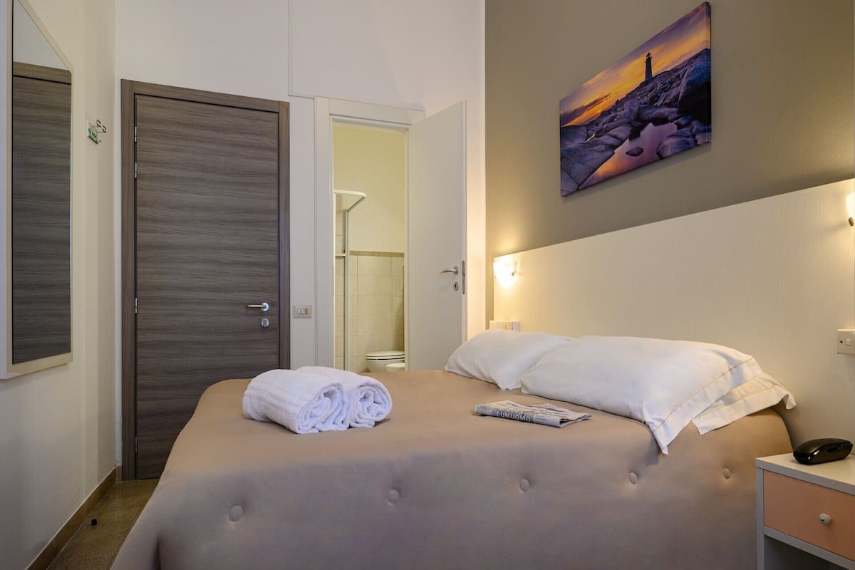 A hotel room with a bed, a nightstand, a painting, and a door to a bathroom.