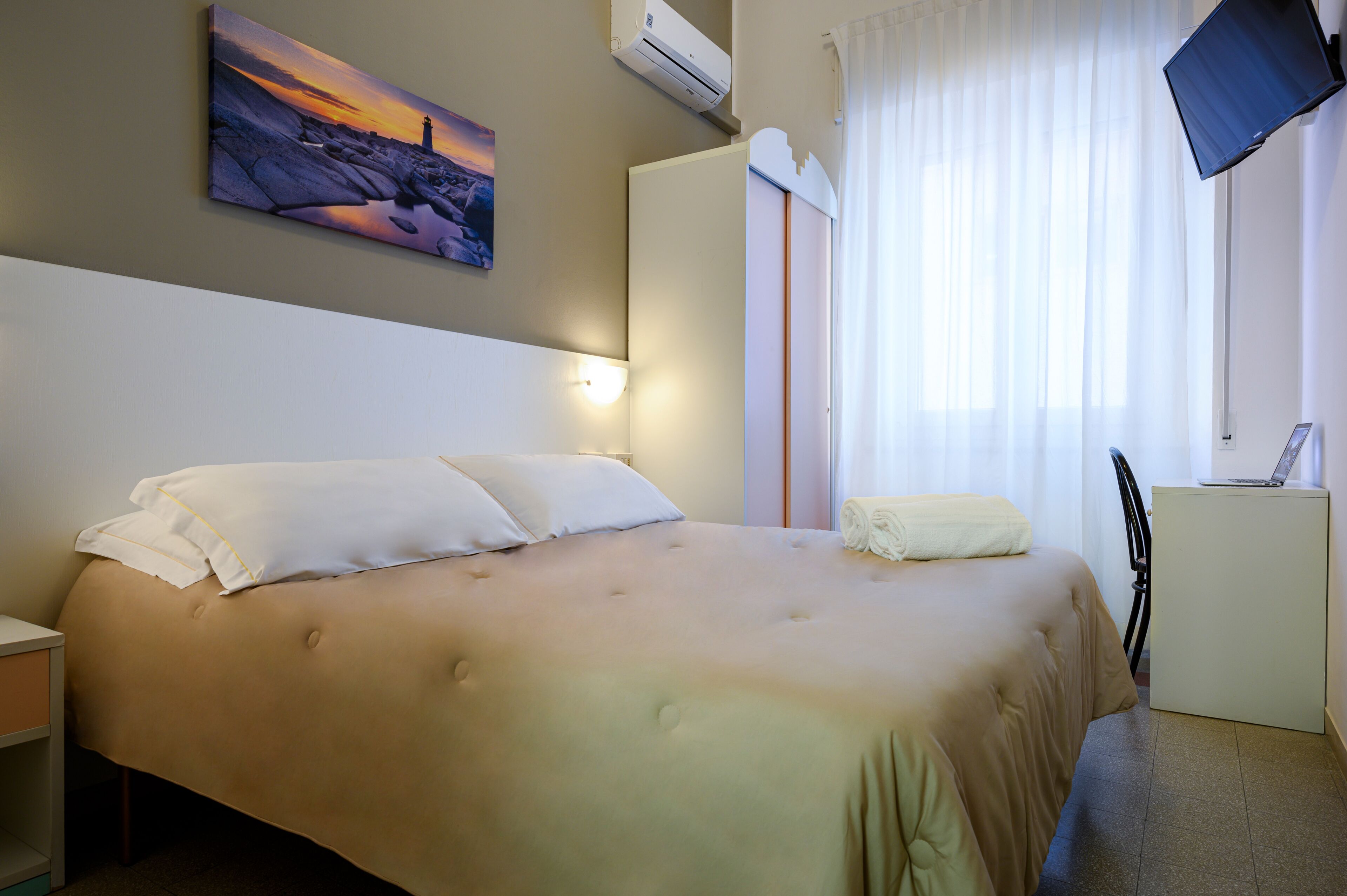 Habitación de hotel con cama, escritorio, televisión y un cuadro en la pared.
