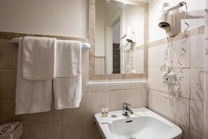 A bathroom with two towels hanging on a rack, a sink with toiletries, a mirror, and a hairdryer mounted on the wall. - Amadei Hotel Blumen (Pesaro)