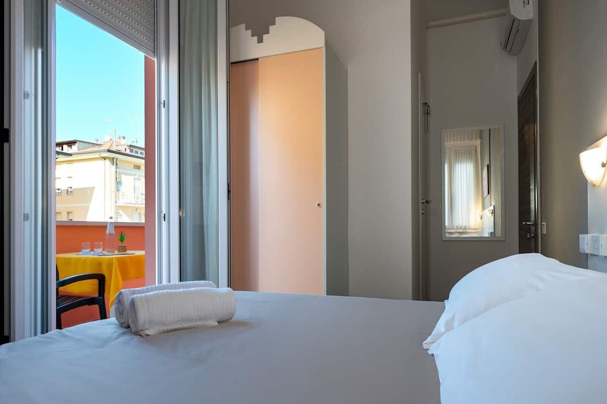 A hotel room with a large bed, a balcony with a table and chairs, and a door leading to another room.