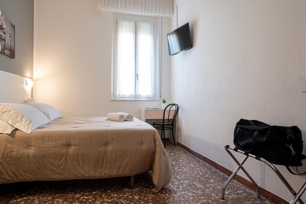 Habitación de hotel con cama, escritorio, silla, televisor y bolso sobre una silla.