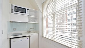 A compact kitchenette with a microwave, shelves, and a refrigerator.