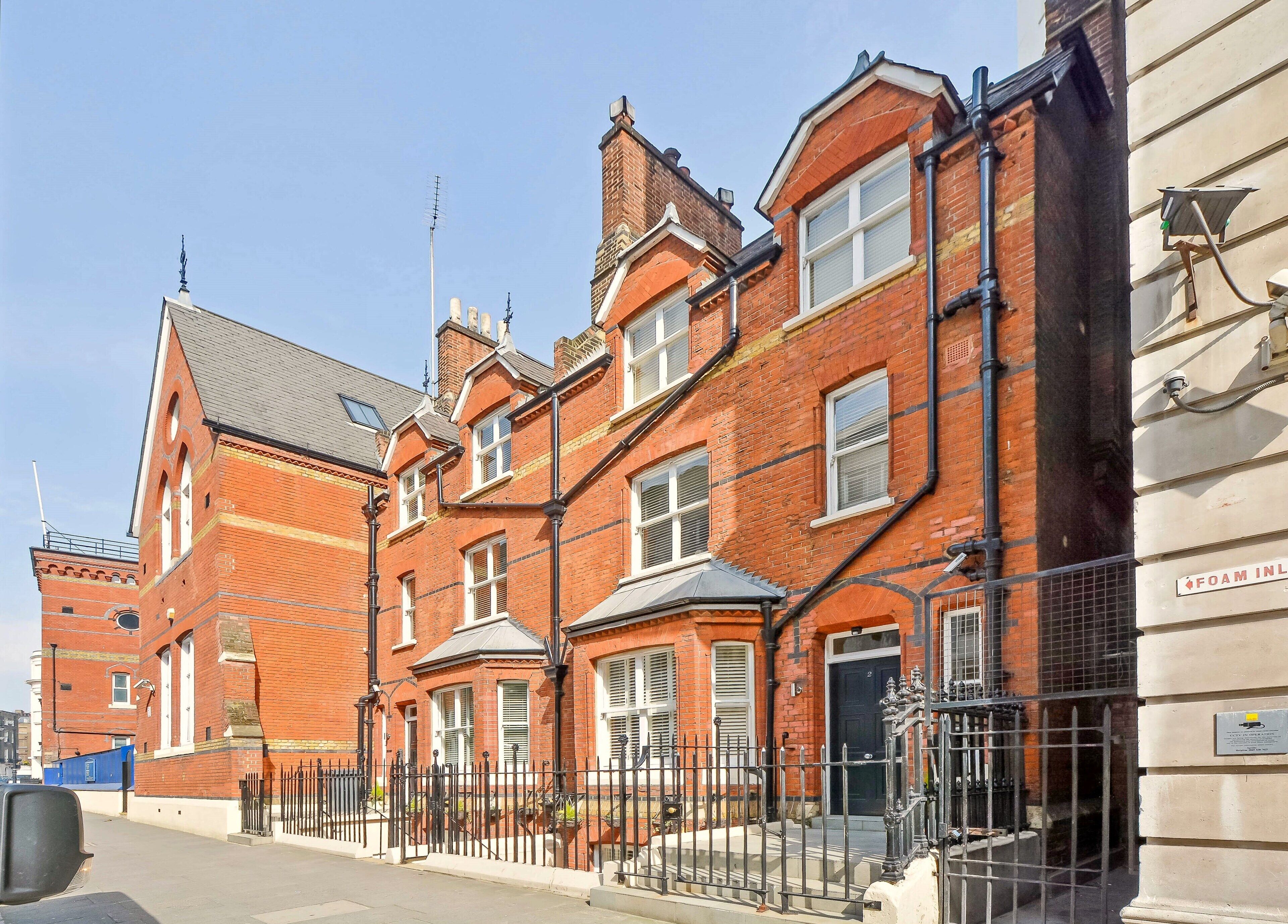 A row of red brick townhouses with white window frames and black metal railings.
