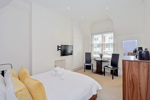Quarto de hotel moderno com uma cama grande, uma escrivaninha com cadeira, televisão e janela com persianas.