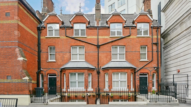 A red brick townhouse with a symmetrical facade, multiple windows, and a central chimney.