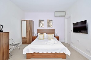 Quarto bem arrumado com cama, guarda-roupa de madeira e televisão na parede.