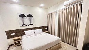 A modern hotel room with a large bed, a headboard with a geometric design, a wall-mounted air conditioner, and a window with curtains. - The Paving Villa (Canggu)