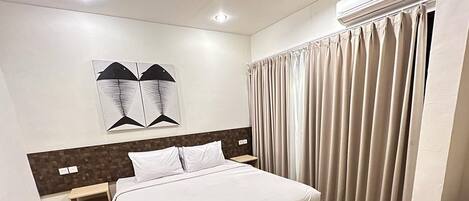 Une chambre d’hôtel moderne dotée d’un grand lit, d’une tête de lit au motif géométrique, d’un climatiseur fixé au mur et d’une fenêtre avec des rideaux.