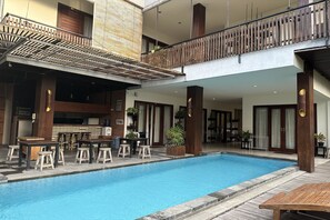 Ein Poolbereich mit Bar und Sitzgelegenheiten, Holzgeländern und Topfpflanzen.