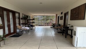 A spacious hallway with tiled flooring, wooden doors, and a seating area with chairs and tables. - The Paving Villa (Canggu)