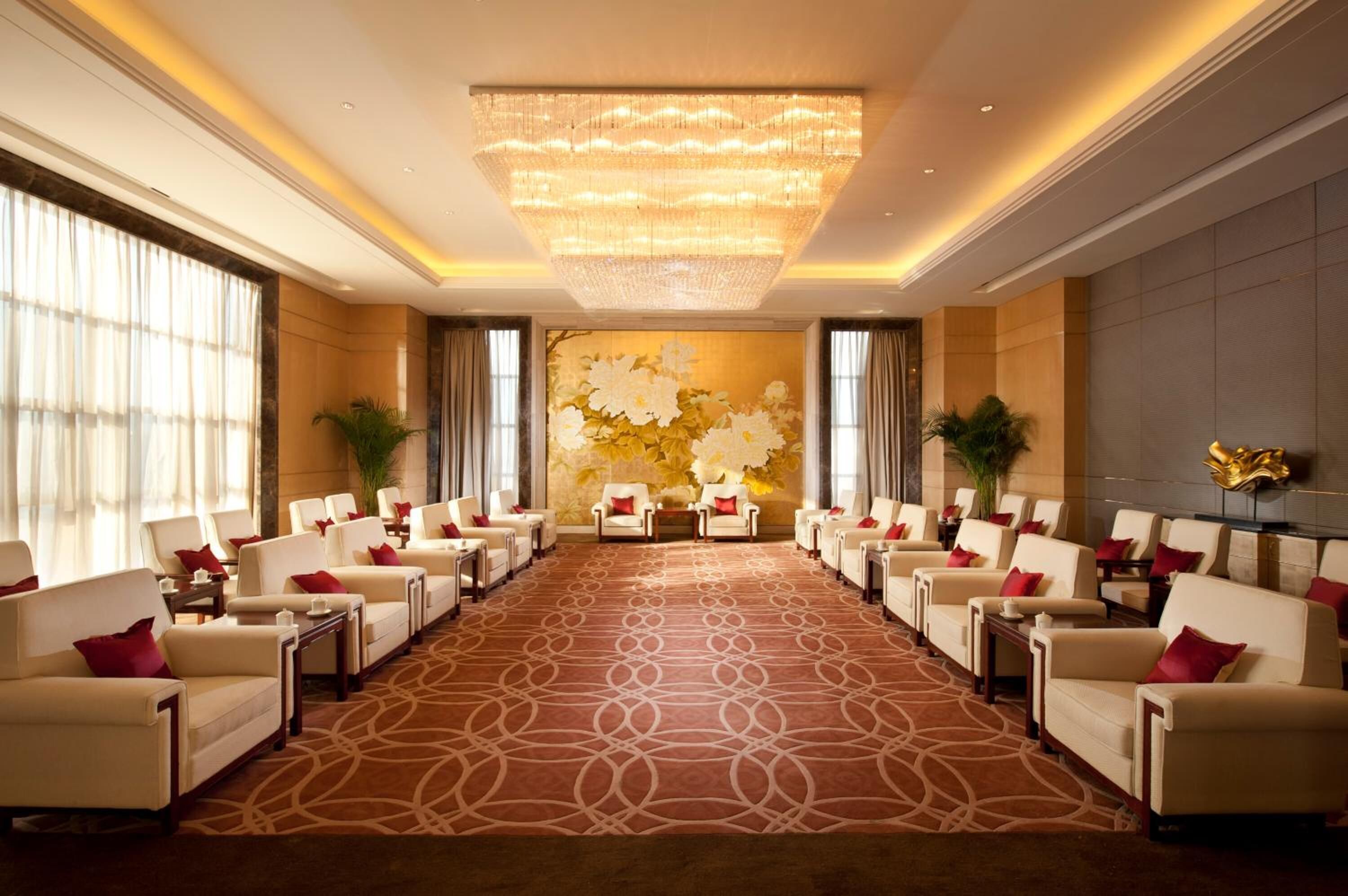 Un hall d’entrée spacieux, doté d’un tapis à motifs, de rangées de sièges et d’un grand lustre.