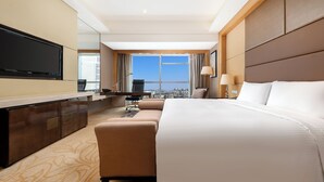 Habitación de hotel con una cama grande, un escritorio, un televisor de pantalla plana, un sofá y vistas a la ciudad.