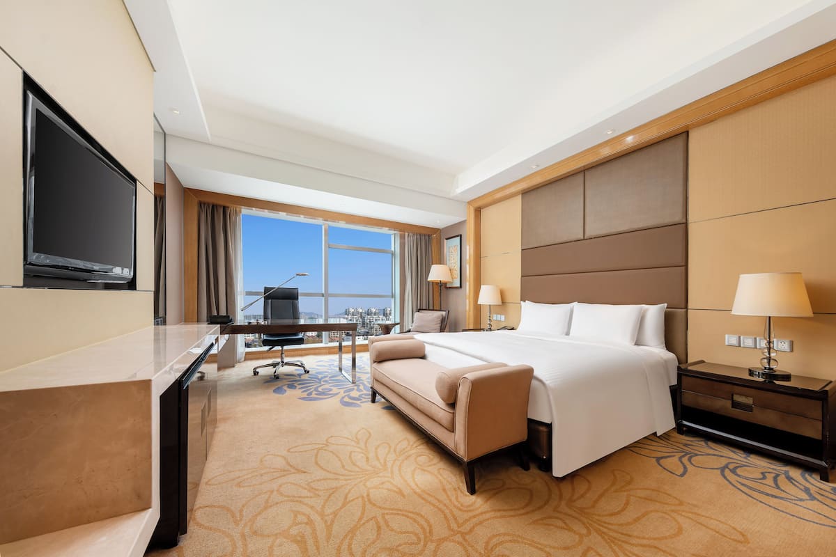 A hotel room with a bed, a desk, a TV, and a view of the city.
