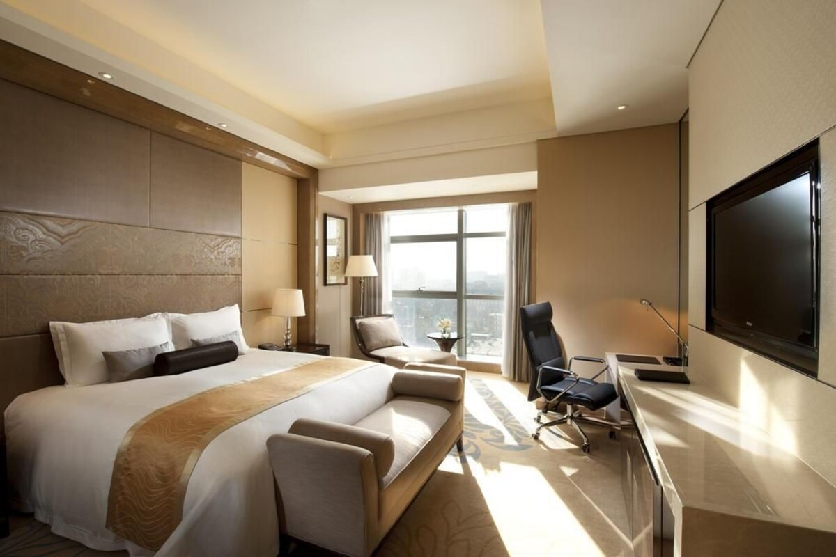 Una habitación de hotel moderna con una cama grande, un escritorio, una silla y un televisor.