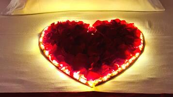 Una cama con un almohadón que dice "you & me beach hotel" y una lámpara decorativa con forma de corazón sobre la cama.
