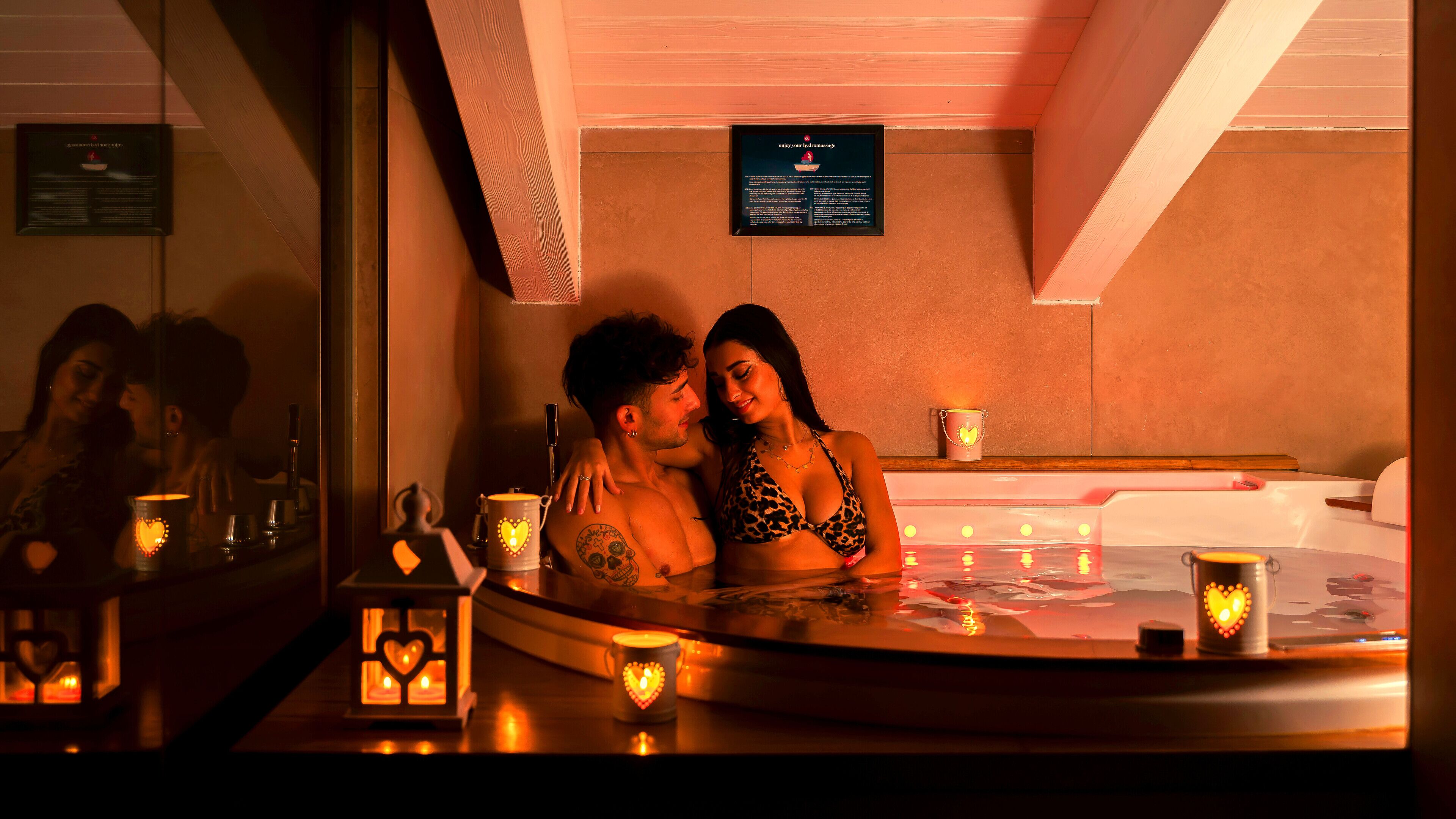 Una pareja en un jacuzzi, con velas en forma de corazón y un cartel sobre ellos.