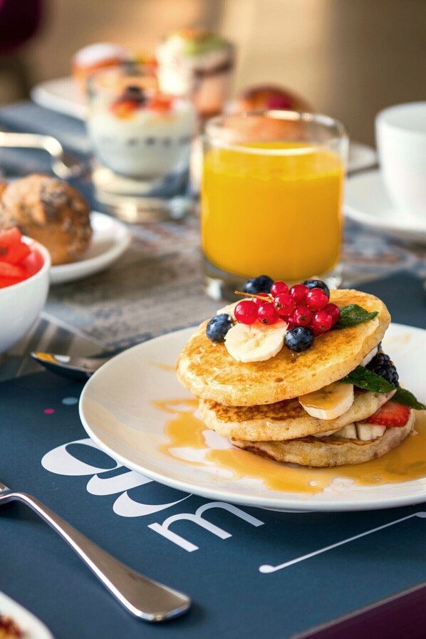 A breakfast setting with pancakes topped with berries and syrup, a glass of orange juice, and a plate of waffles.