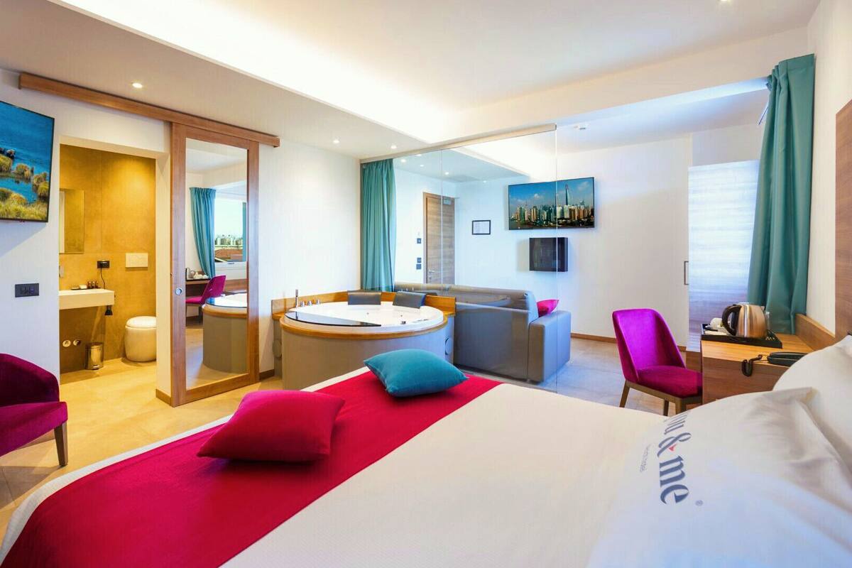 Ein Hotelzimmer mit einem großen Bett, einer Sitzecke inklusive Sofa und Couchtisch, einem separaten Badezimmer und Blick auf die Stadt.
