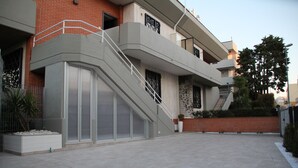 A modern building with a flat roof, a staircase leading to the upper floor, and a small garden area with a potted plant. - Principe (Bari)