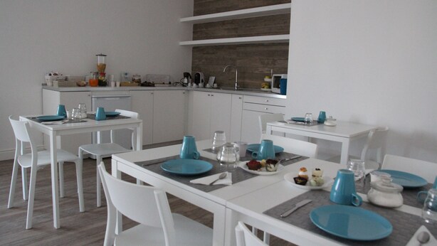 A modern kitchen with white cabinets, a built-in oven, and a coffee machine. There is a dining table set with blue plates and white chairs. - Principe (Bari)