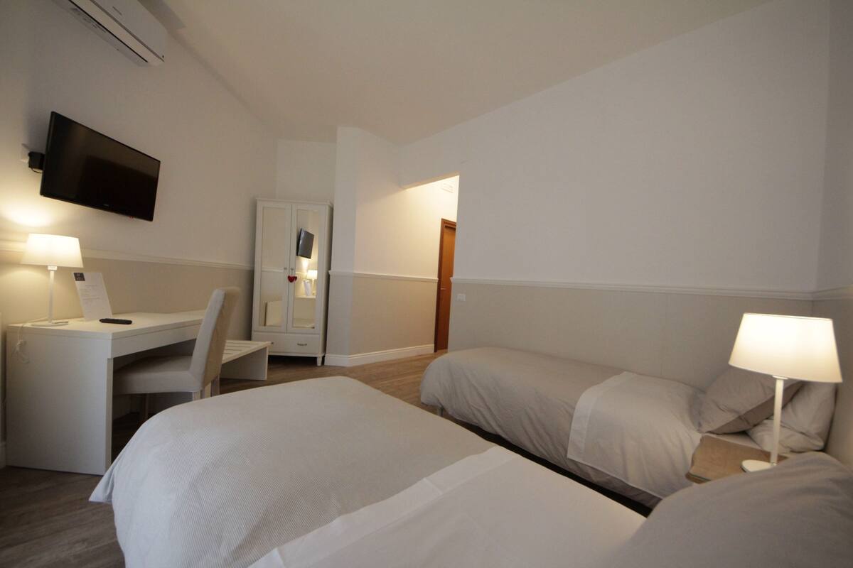 A hotel room with a bed, a desk, a chair, a TV, and a lamp.