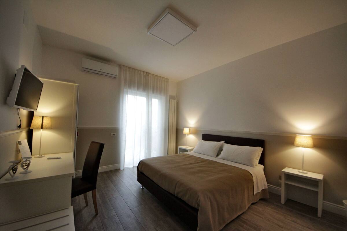 A hotel room with a bed, bedside tables, a TV, and a desk with a chair.