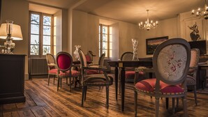 Una habitación con piso de madera, una mesa de comedor, sillas, un candelabro y ventanas amplias.