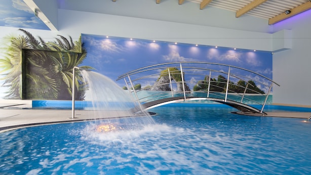 Ein Innenpool mit Wasserfall, umgeben von einer Wandmalerei mit tropischer Landschaft.