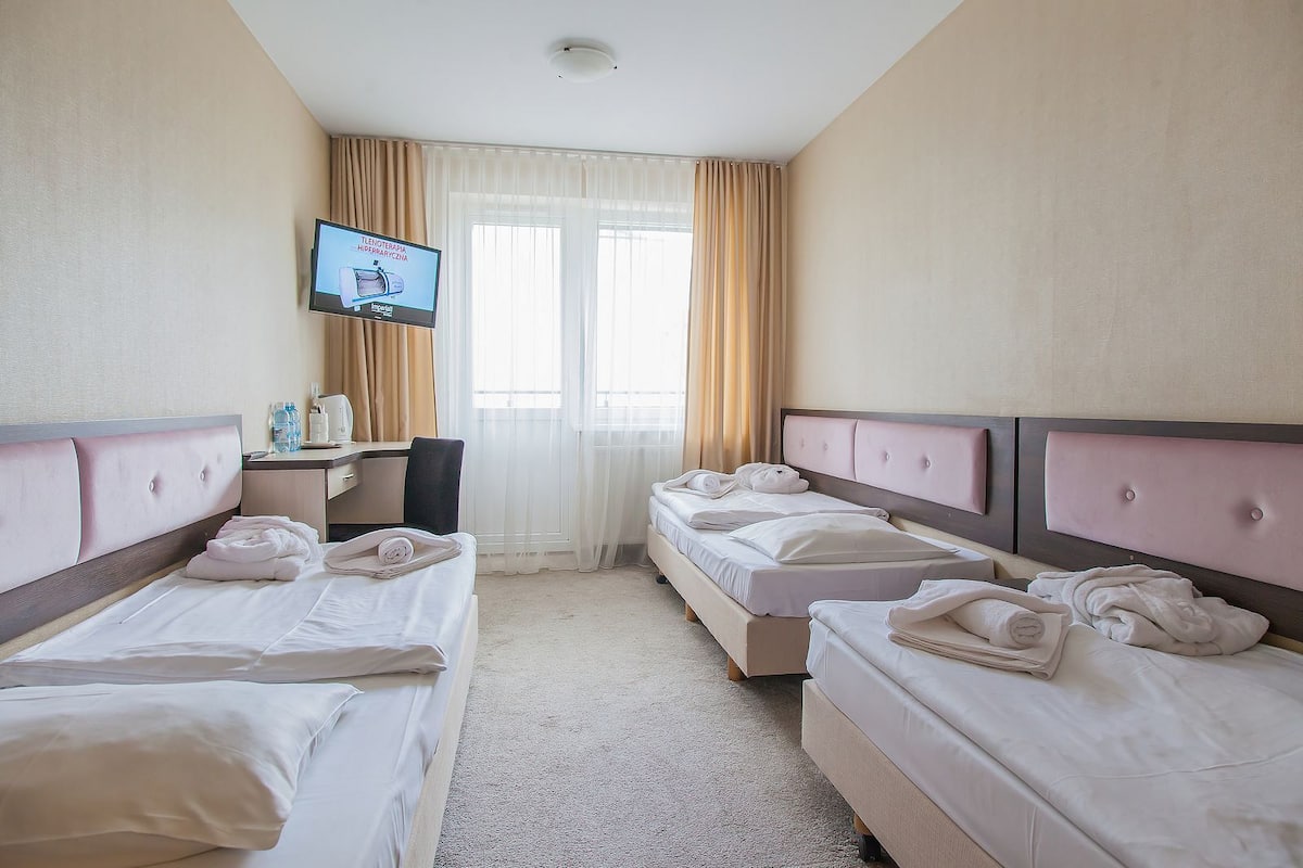 Habitación de hotel con dos camas, un escritorio, un televisor y una ventana con cortinas.