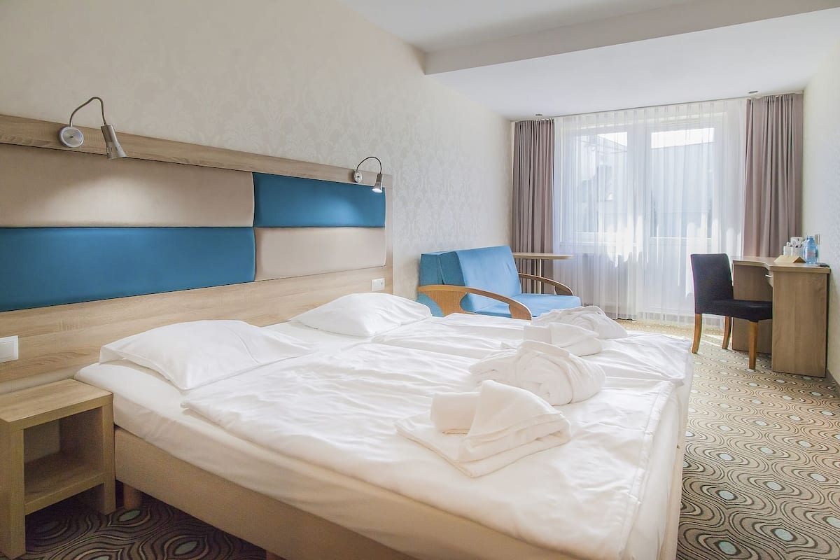 Habitación de hotel con una cama grande, dos sillas, un escritorio y una ventana con cortinas.