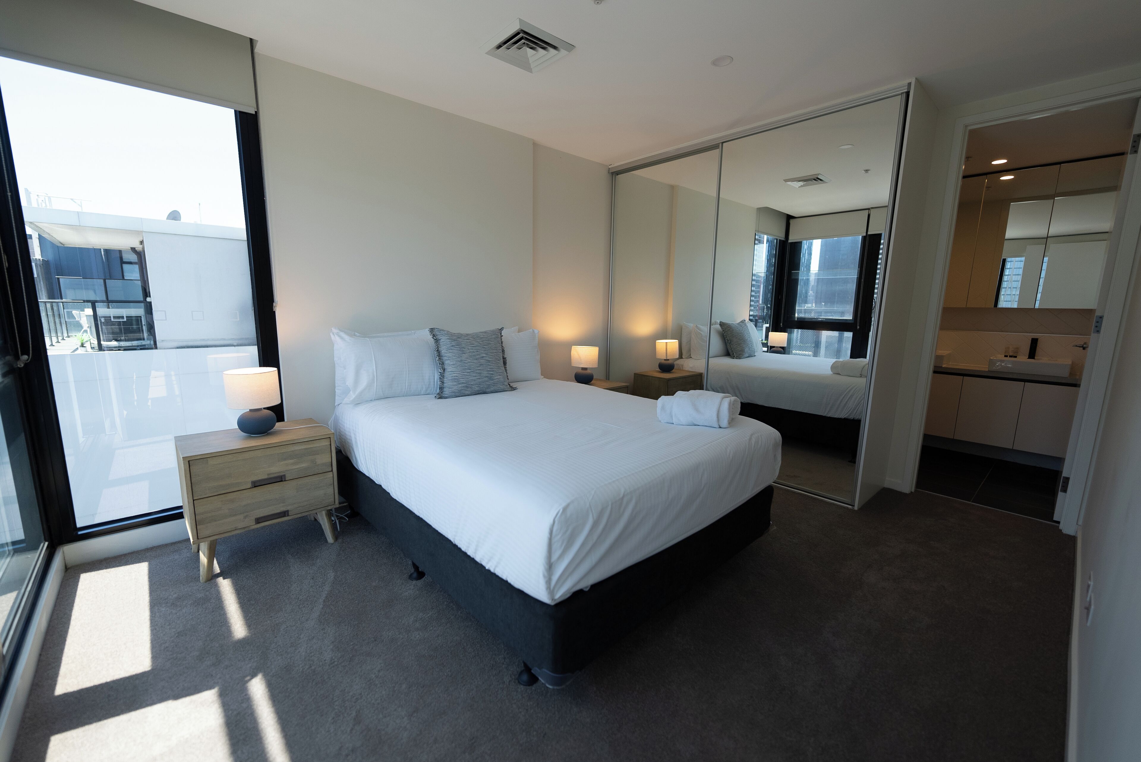 A modern hotel room with a large bed, bedside lamps, a mirror, and a view of the outside.