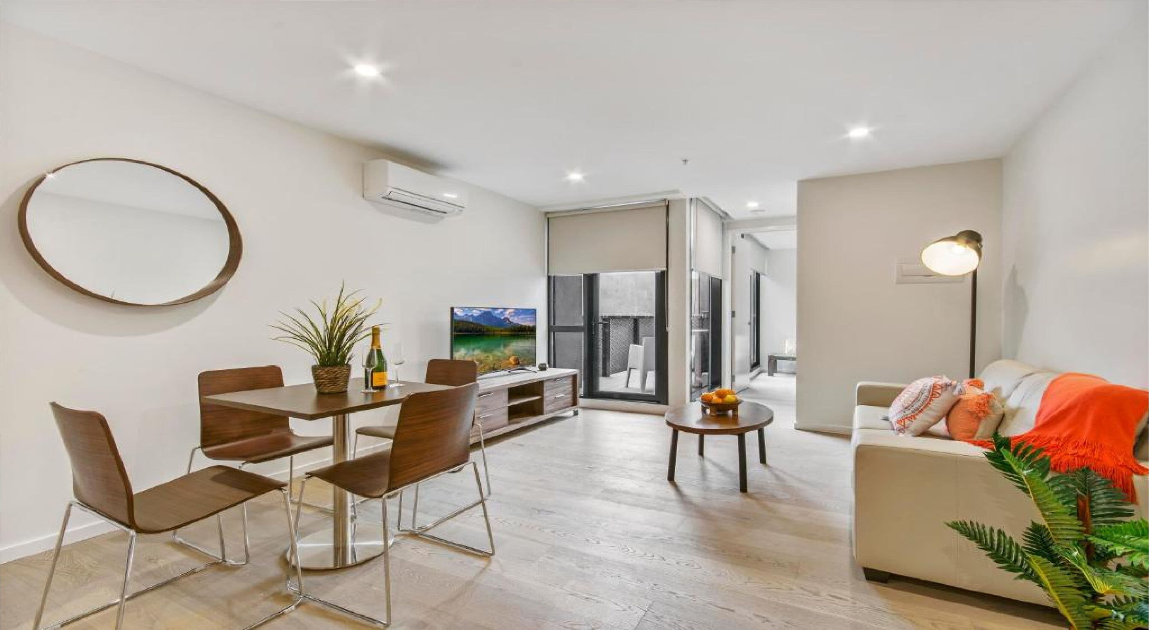 A modern living room with a dining area, a sofa, a TV, and a plant.
