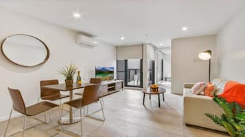 A modern living room with a dining area, a sofa, a TV, and a plant.
