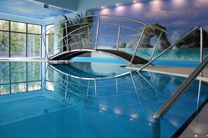Una piscina interior con barrera de cristal y un mural de paisaje tropical.