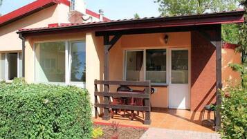 A two-story building with a red roof, large windows, and a covered patio area with a table and chairs.