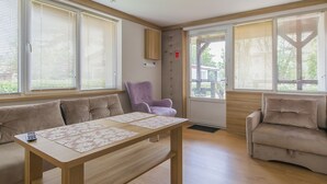 A modern living room with a wooden table, beige sofas, and large windows with blinds. - Imperiall Resort & MediSpa - Cottage (Ustronie Morskie)