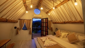 A cozy, rustic room with a wooden ceiling, a bed with white linens, and a view of the outdoors through an open door.