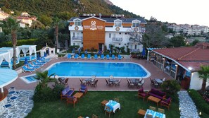 A hotel with a swimming pool, outdoor seating, and a mountain backdrop. - Iksirci Baba Hotel (Fethiye)