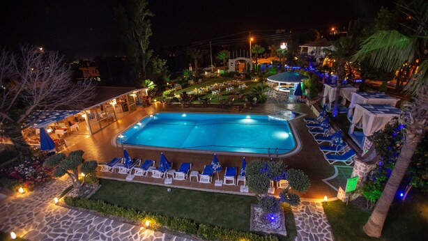 A nighttime view of a hotel with a swimming pool, lounge chairs, and a well-lit outdoor area.