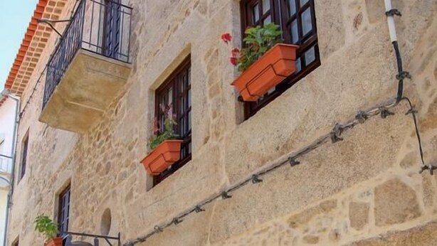 A stone building with multiple windows, some with flower boxes, and a cobblestone street. - Casa d'Acha (Idanha-a-Nova)