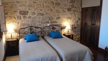 Una habitación con dos camas, paredes de piedra, vigas de madera y una puerta de madera.