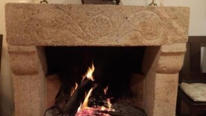 A stone fireplace with a fire burning inside, framed by a simple mantelpiece and two candles. - Casa d'Acha (Idanha-a-Nova)