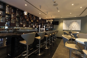 A bar area with multiple stools, a counter with bottles, and a wall-mounted TV. - Premier Inn Abu Dhabi Airport Hotel (Abu Dhabi)