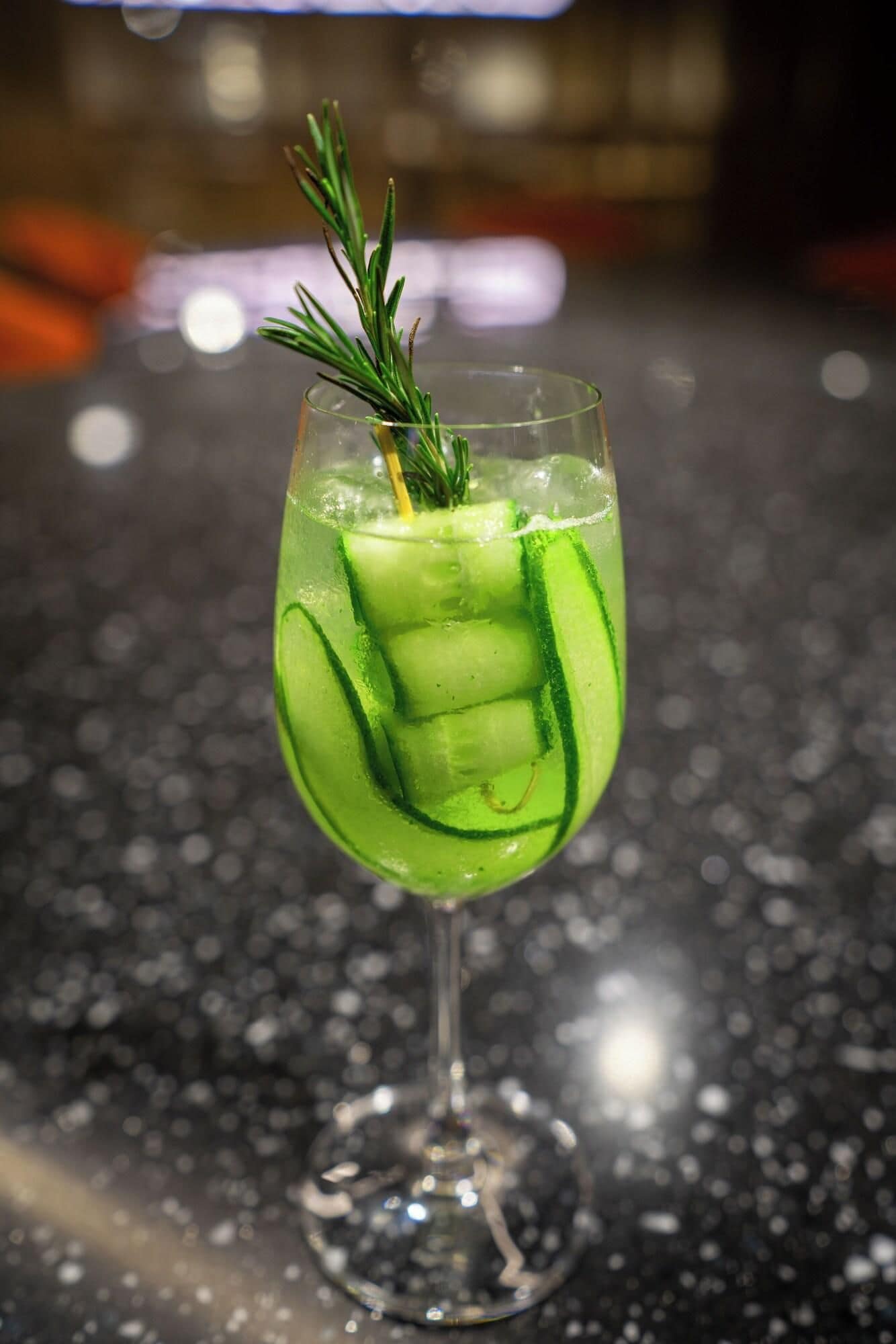 Et cocktailglas med et agurkeskive og en kvist rosmarin.