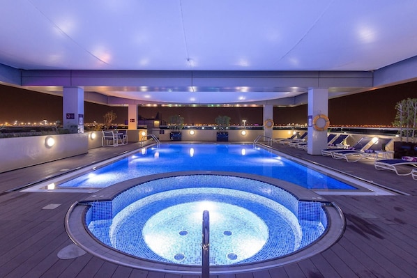 A large indoor swimming pool with a hot tub in the center, surrounded by lounge chairs and a bar area.