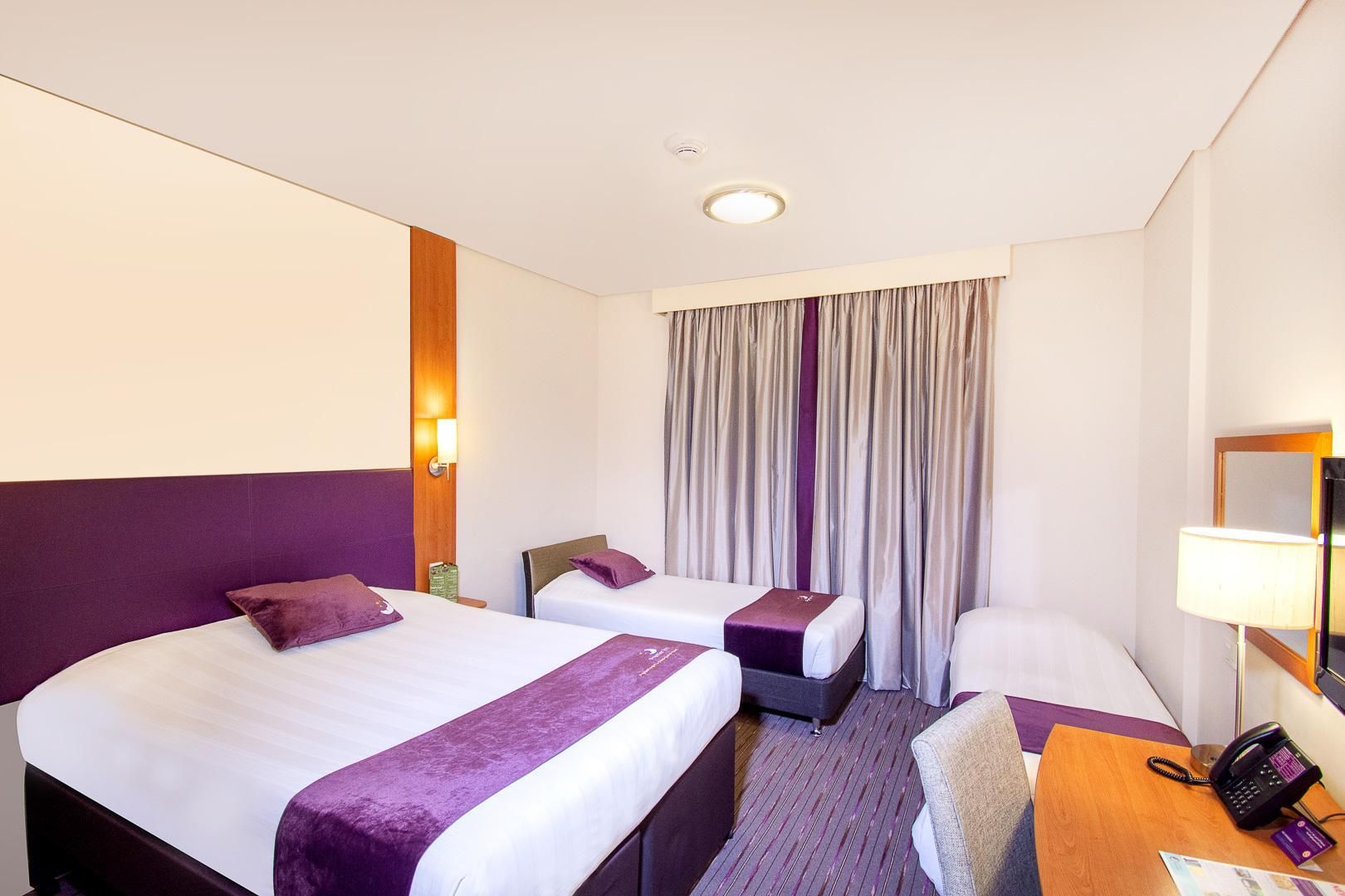 Habitación de hotel con dos camas, un escritorio, una silla, un teléfono y una ventana con cortinas.