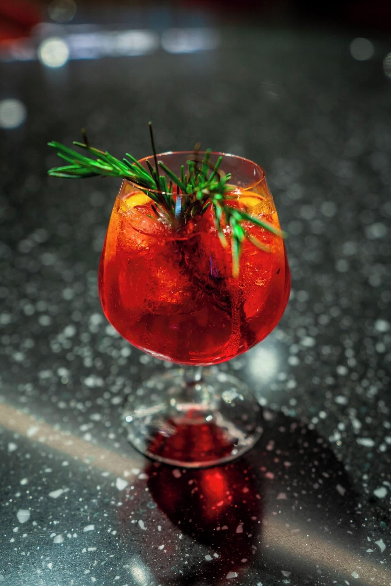 Ein Cocktail im Glas mit Rosmarinzweig, Eiswürfeln und dunklem Hintergrund.